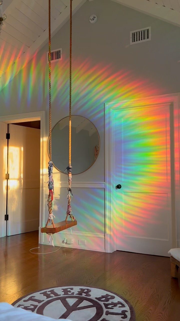 Wooden swing hanging in a room with a rainbow light projection on the wall