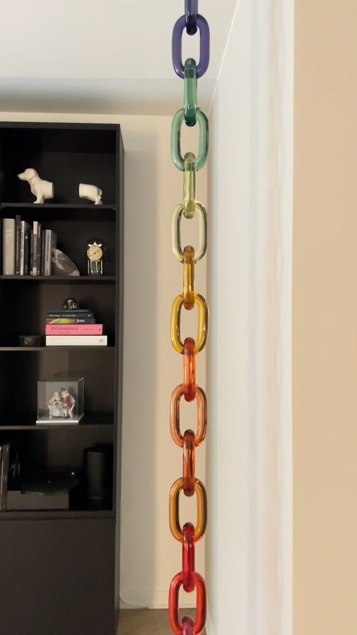 Colorful translucent acrylic chain links hanging vertically next to a black bookshelf.