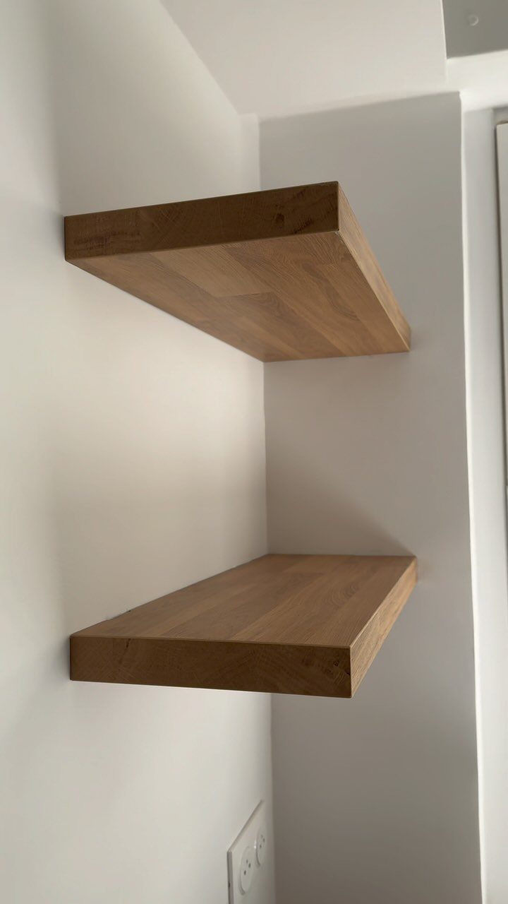 Two light-brown wooden floating shelves mounted in a white room corner.