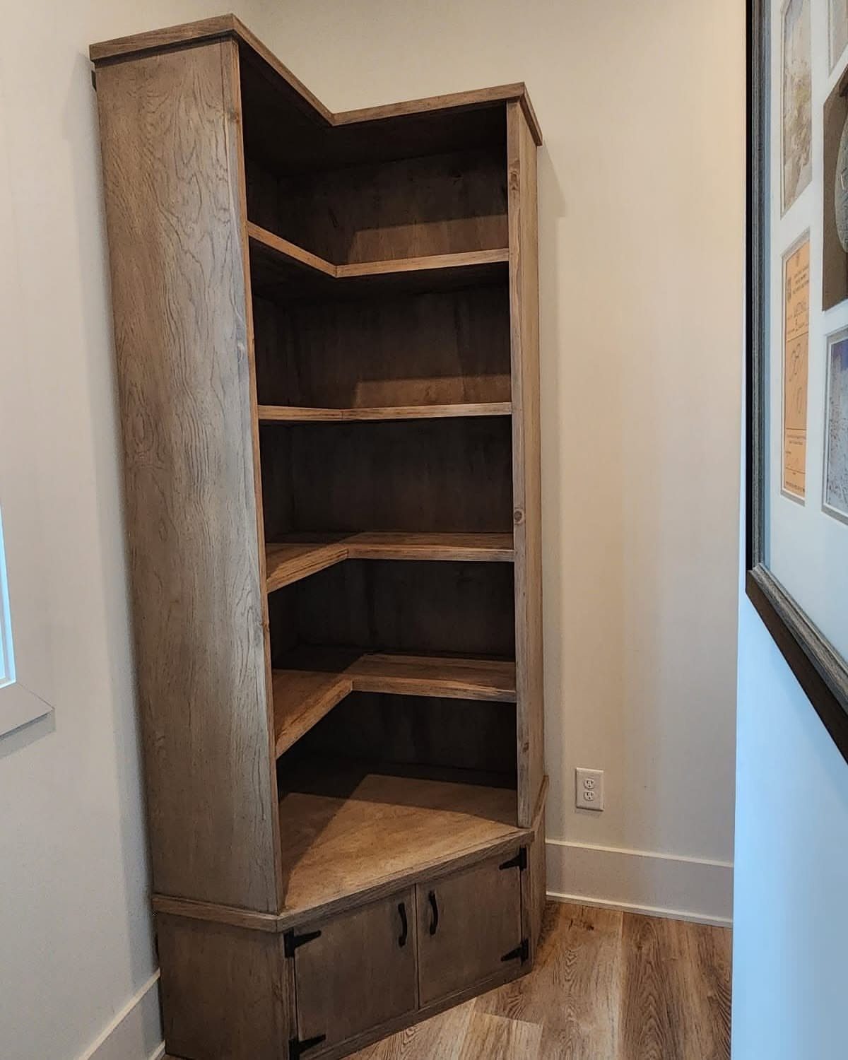 Tall rustic wooden corner bookshelf with open shelves and a bottom storage cabinet.