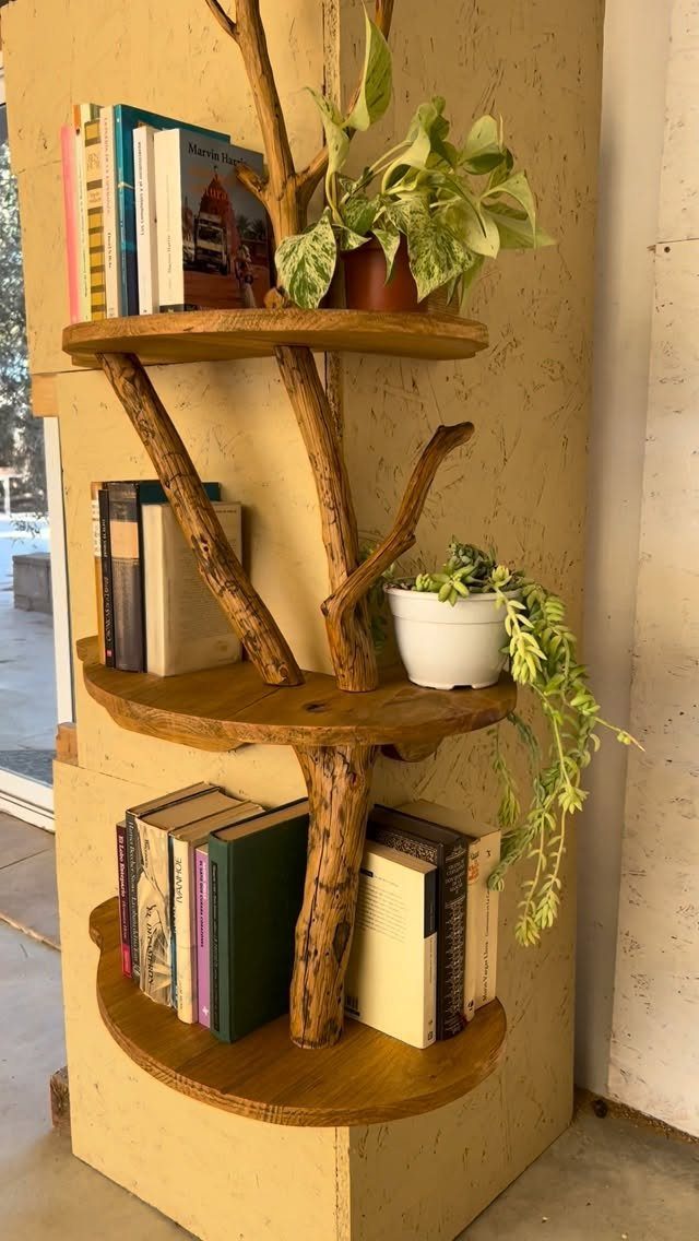 Tree-shaped wooden corner bookshelf with natural branches holding books and potted plants.
