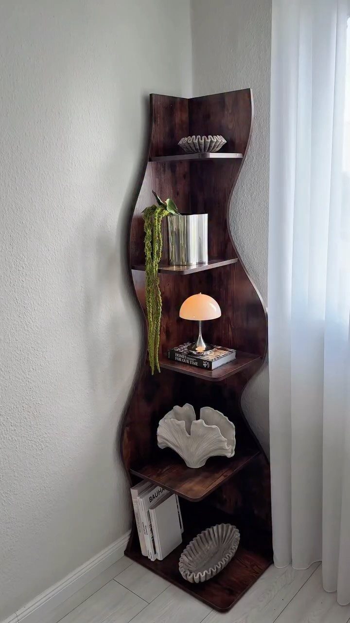 Dark brown wooden triangular corner bookshelf with curved edges and decorative home accessories.