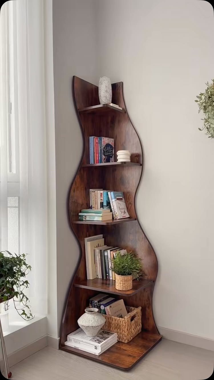 Wavy dark wood corner bookshelf holding books and plants against a white wall.