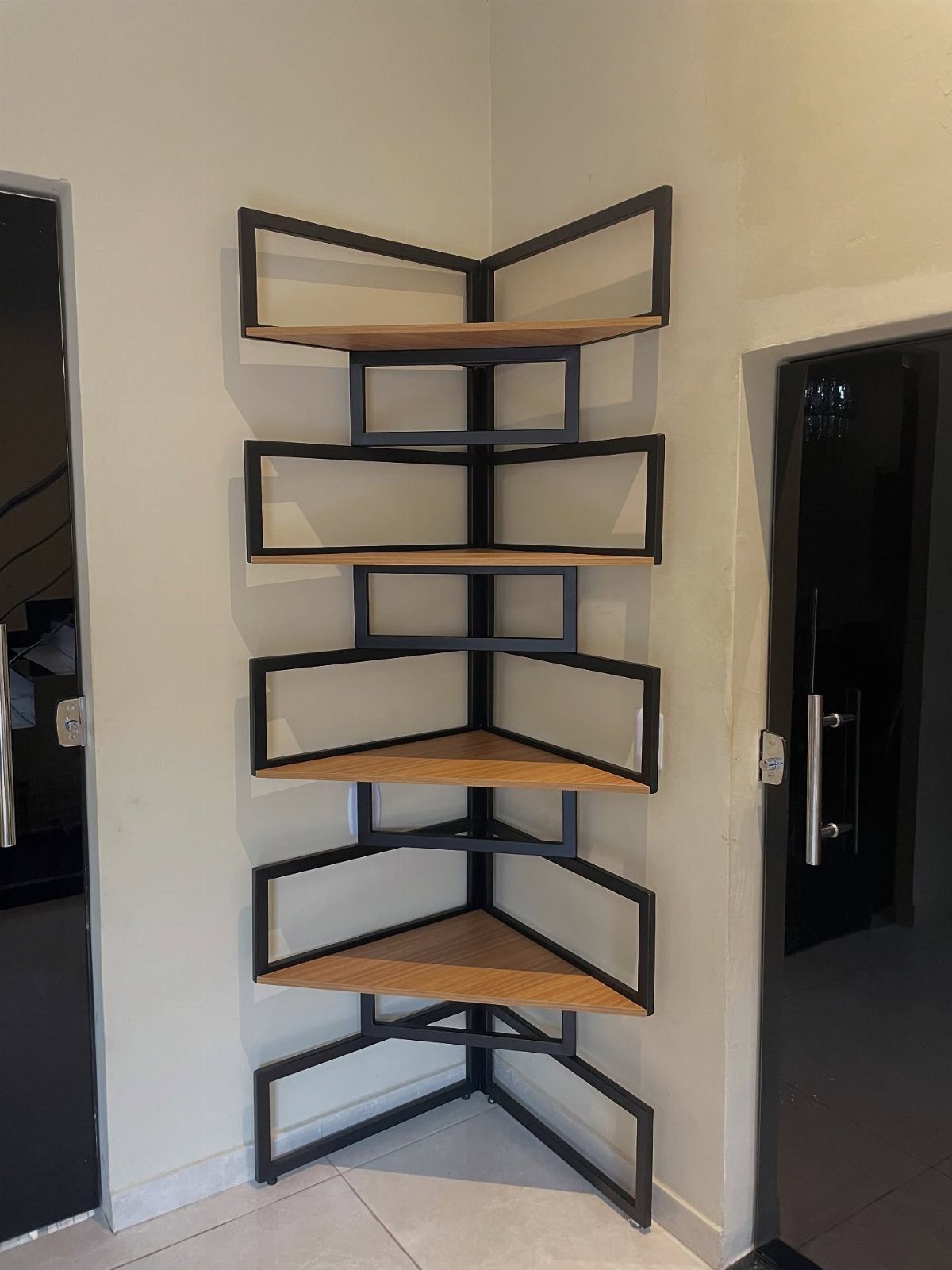 Zig-zagging corner bookshelf with black metal frames and light brown wooden shelves.