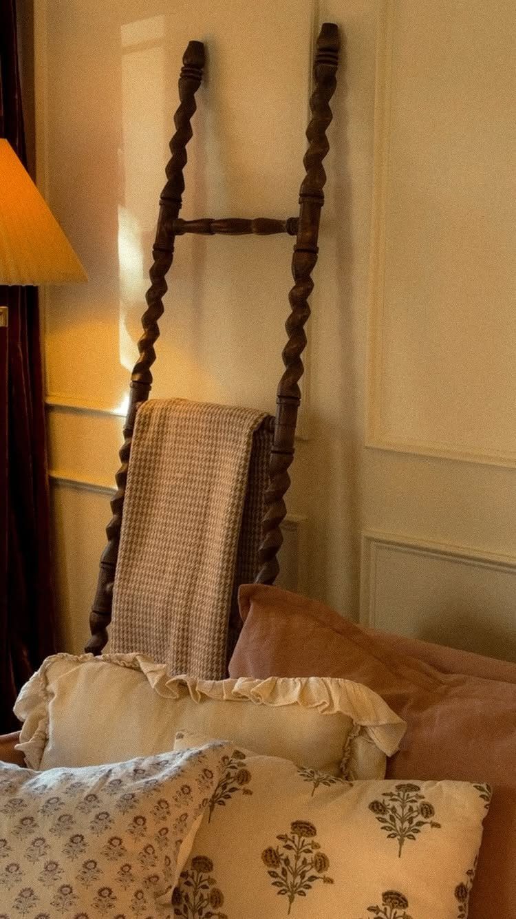 Wooden twisted blanket ladder leaning against a wall with a beige throw blanket.