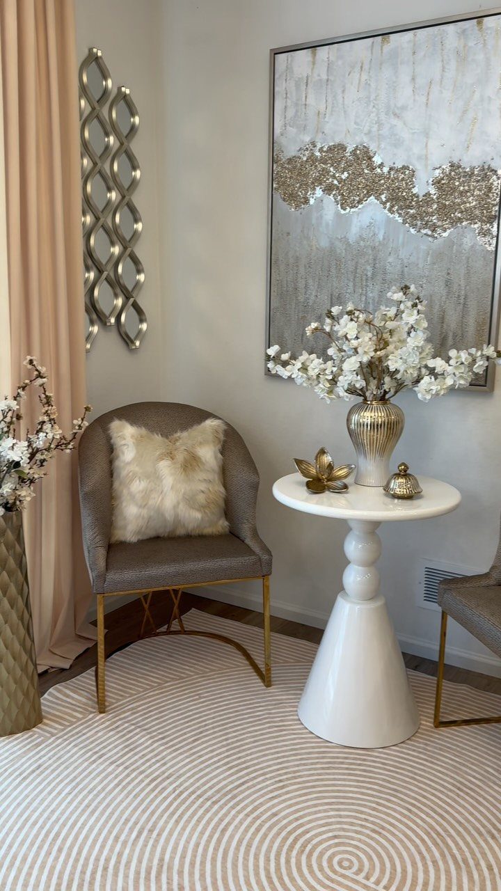 White round accent table with flowers next to a grey armchair in a corner.