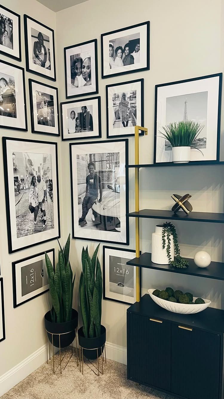 Gallery wall of black and white photos in a room corner with plants.