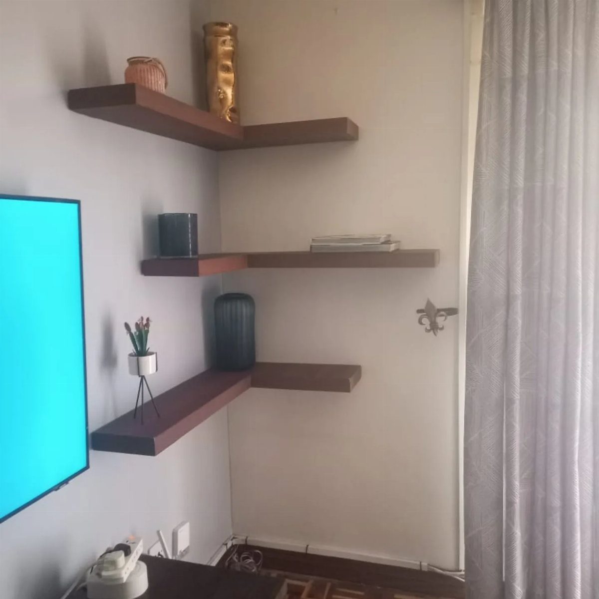 Brown L-shaped floating shelves in a corner holding vases and small decorative items.