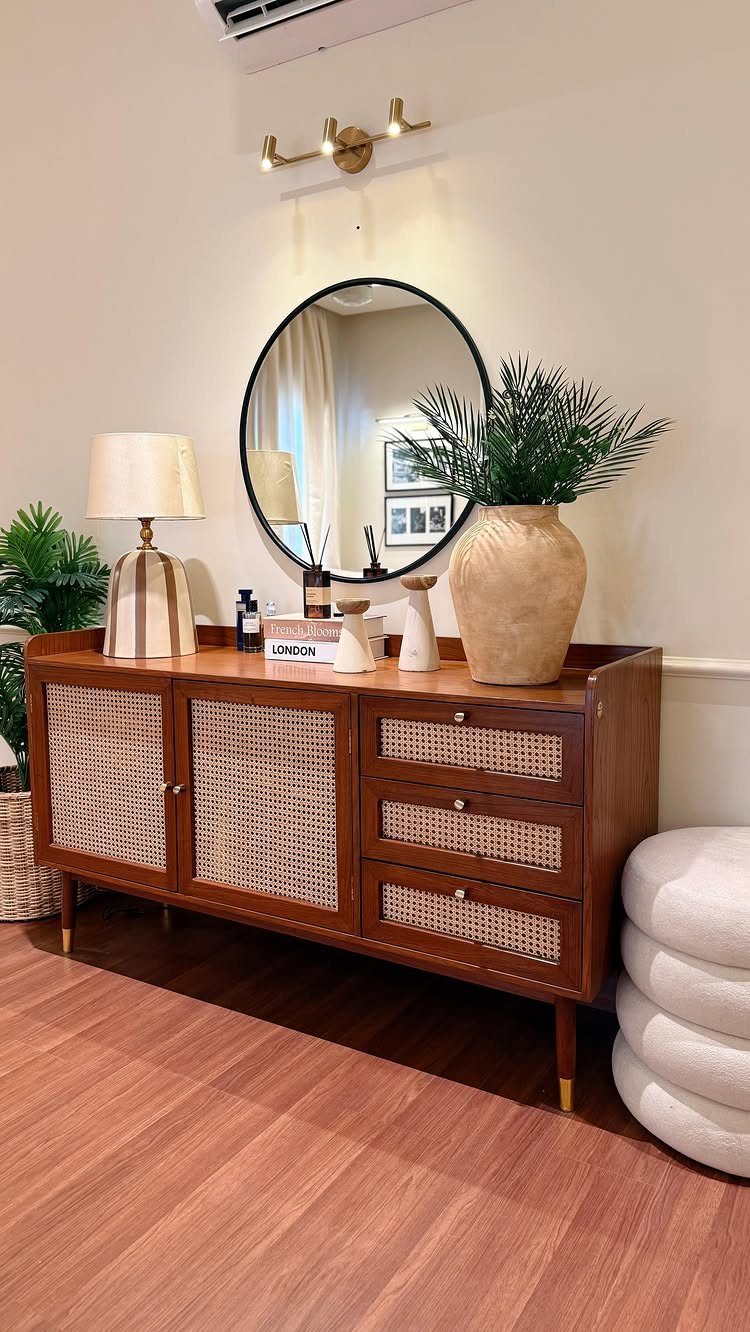 Wooden console table with cane detailing, a round mirror, and decorative vases.