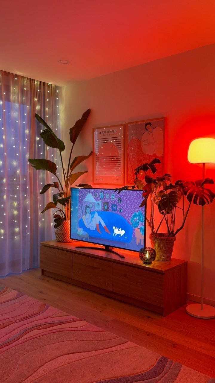 White floor lamp casting orange light next to a wooden TV stand and plants.