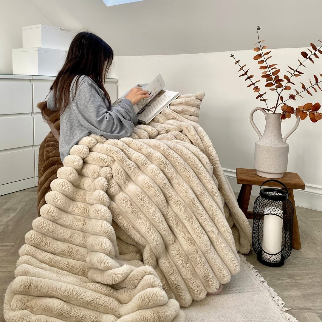 Woman reading a book while wrapped in a thick cream ribbed throw blanket