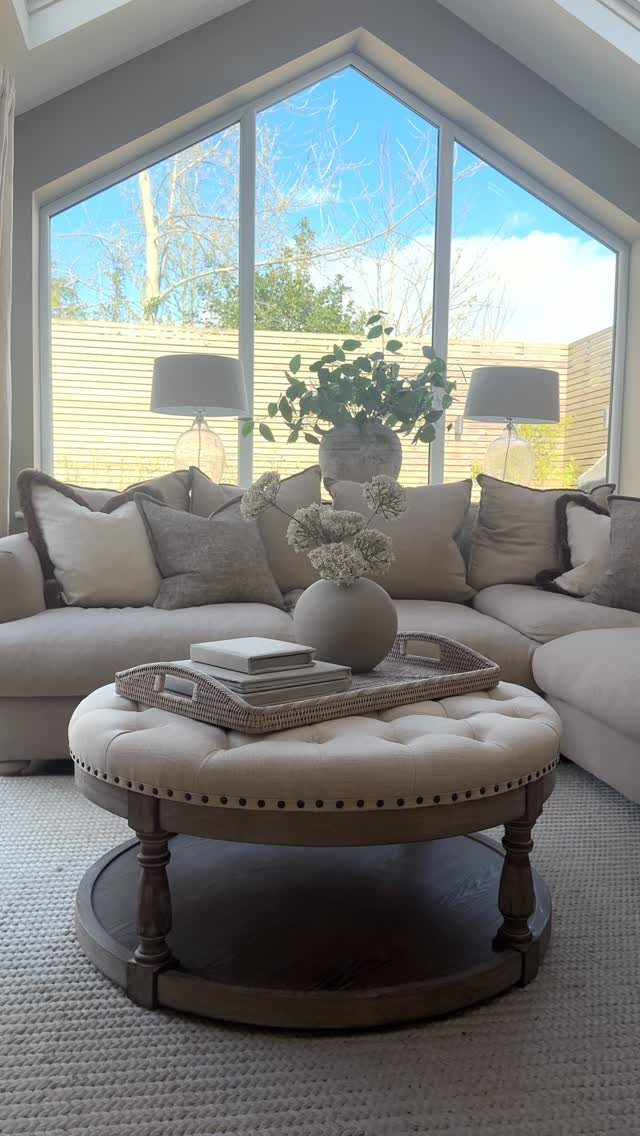 Round tufted cream ottoman with a wooden base and a decorative tray on top.