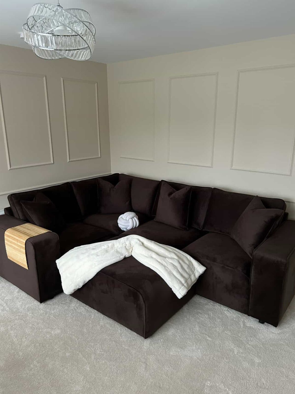 Dark brown velvet sectional sofa with white blankets in a minimalist living room.