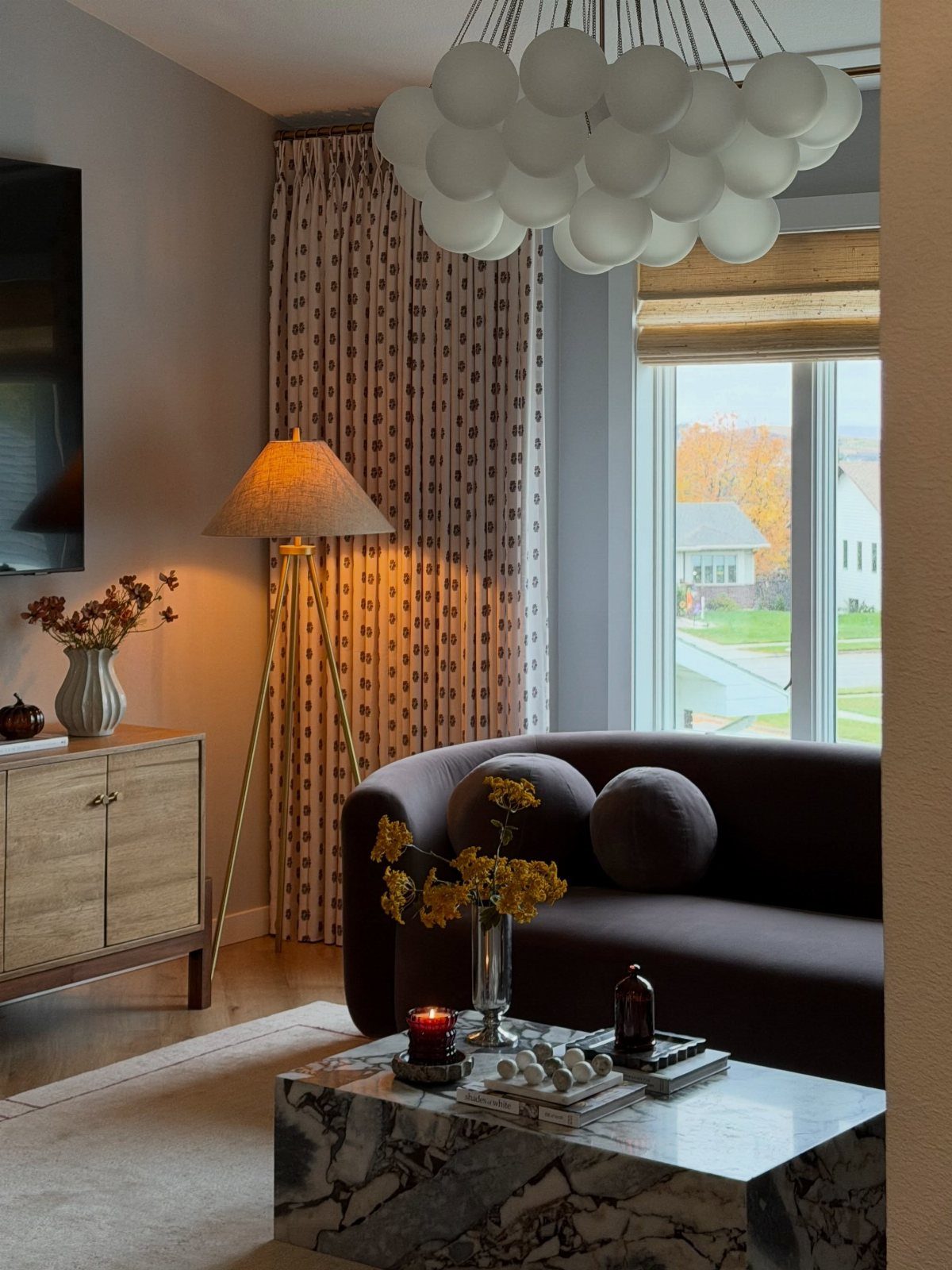 Curved dark brown couch in a modern living room with marble table and bubble chandelier