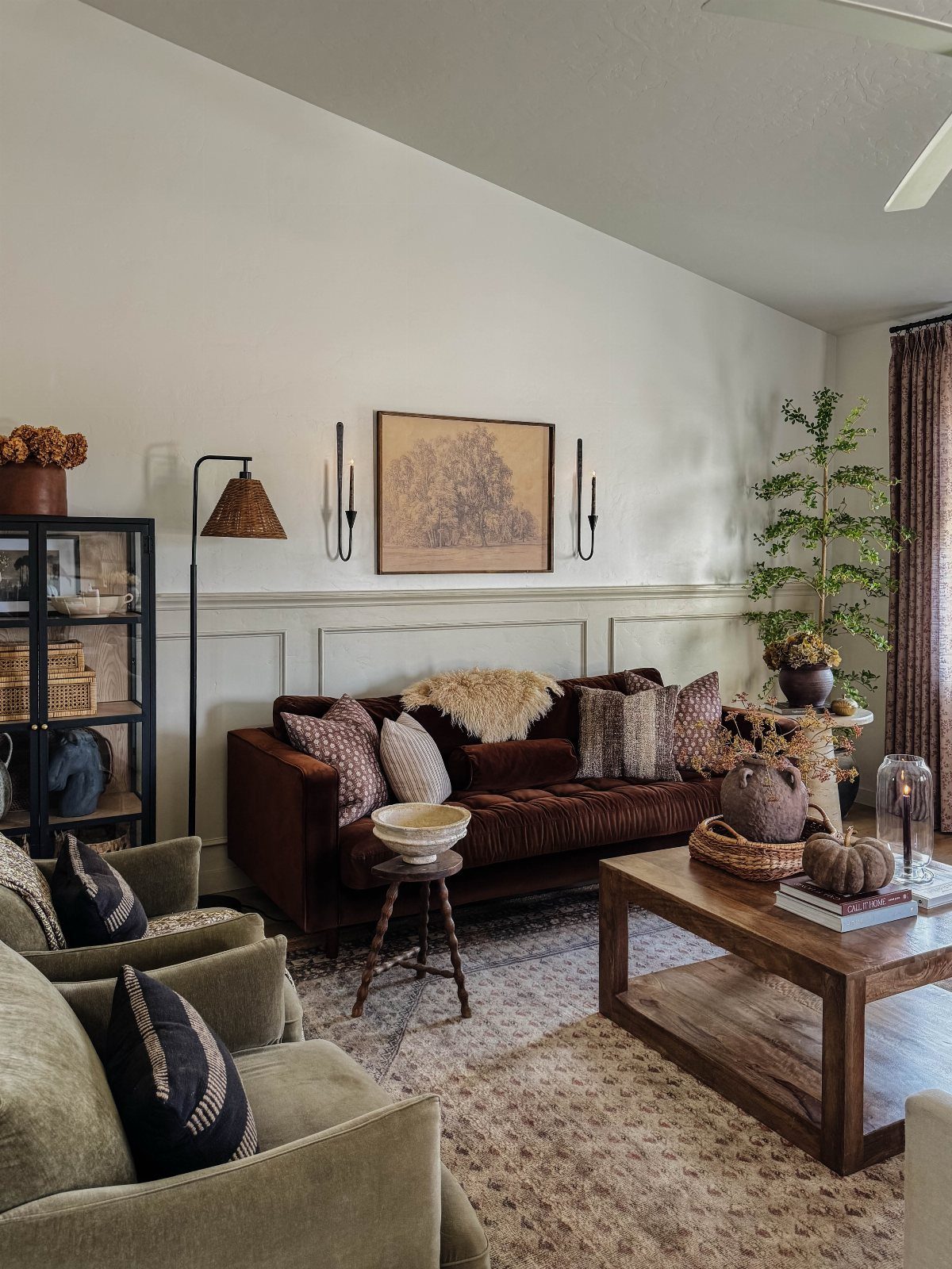 Dark brown velvet couch in a living room with olive green armchairs and wooden furniture.