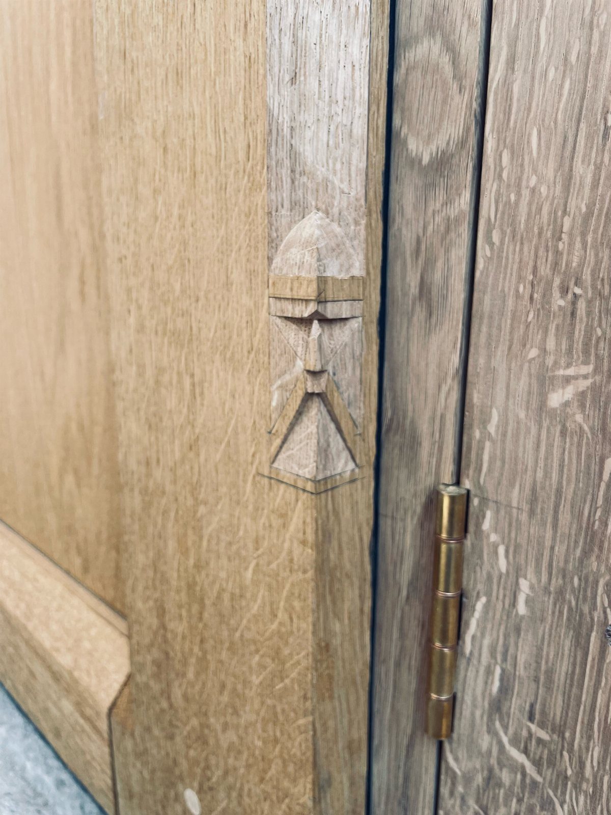 Wooden door frame with a carved decorative detail and a brass hinge