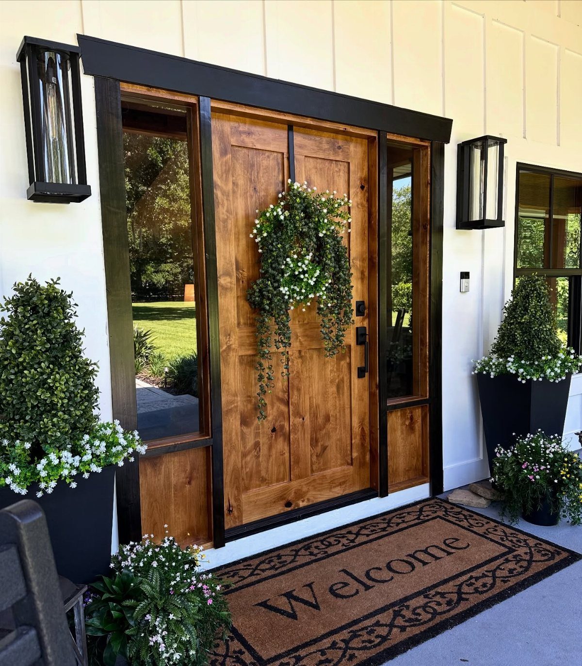 Wooden front door with black trim, sidelights, and a welcome mat on a porch.