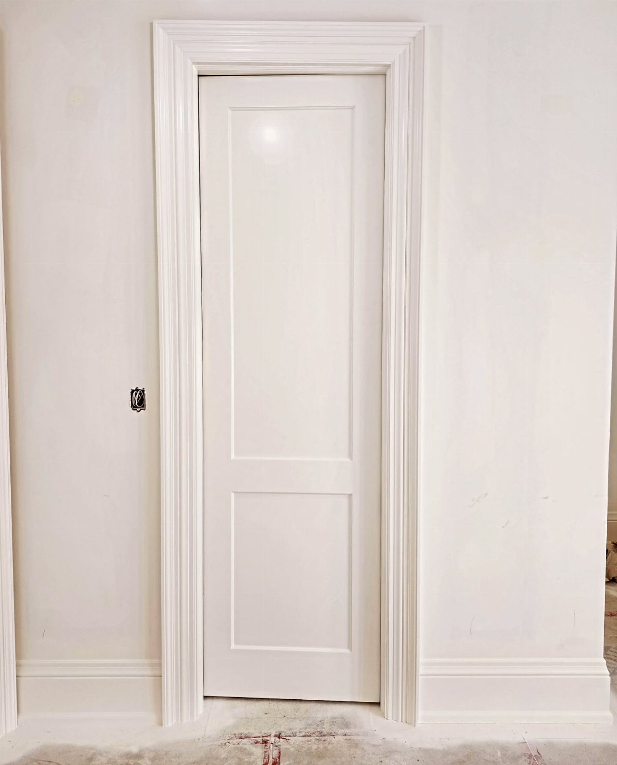 White interior door with ornate multi-layered wooden trim and white baseboards.
