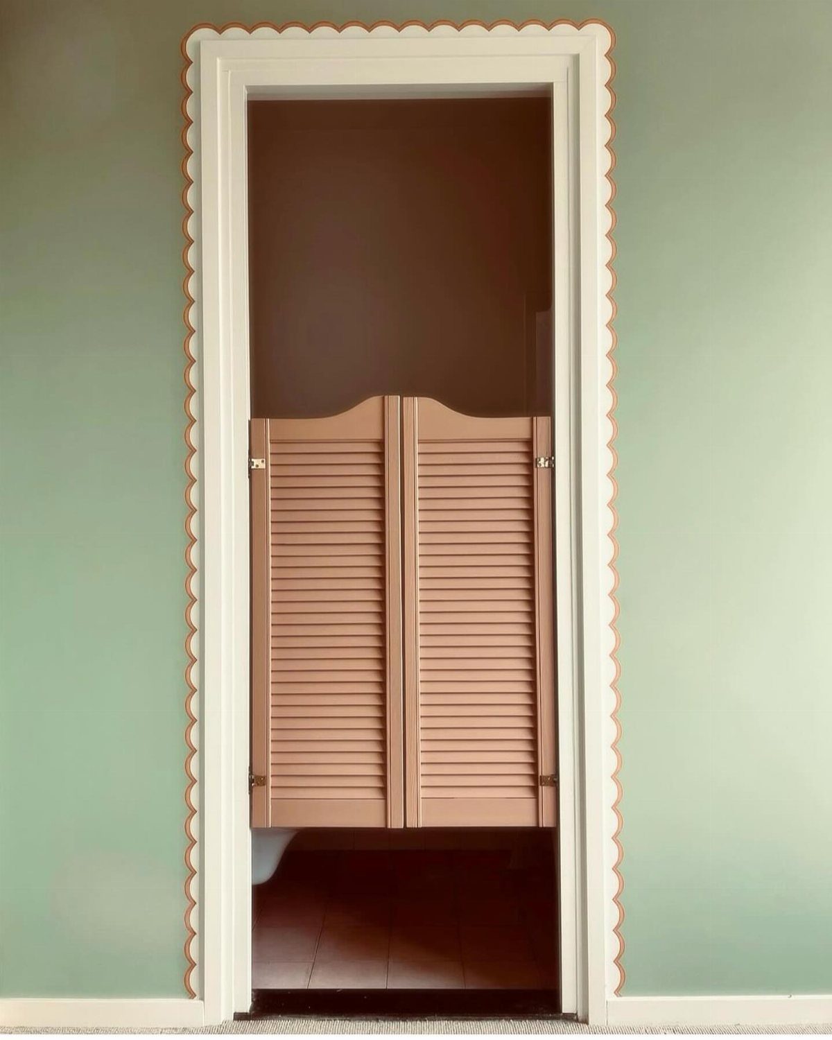 White door frame with a tan scalloped wallpaper border trim on green walls
