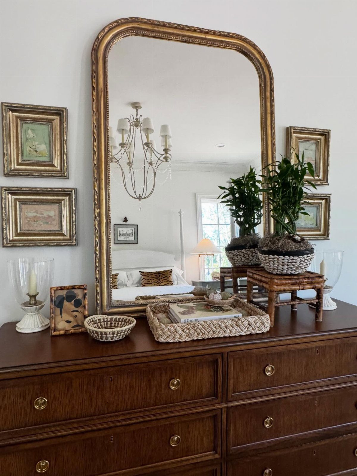 Dark wood dresser with gold-framed mirror and framed artwork on the white wall.