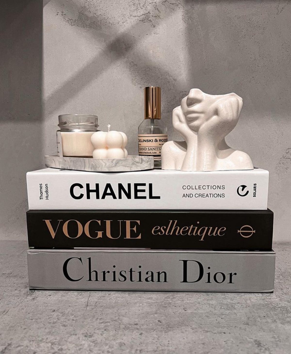 Stacked fashion coffee table books with a white bust and candle on top