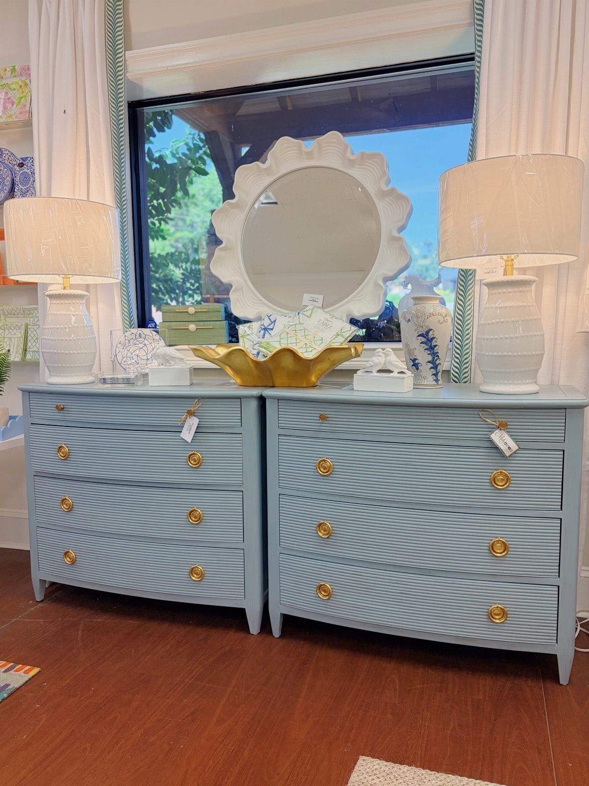 Light blue dressers decorated with white lamps, a scalloped mirror, and seashells.