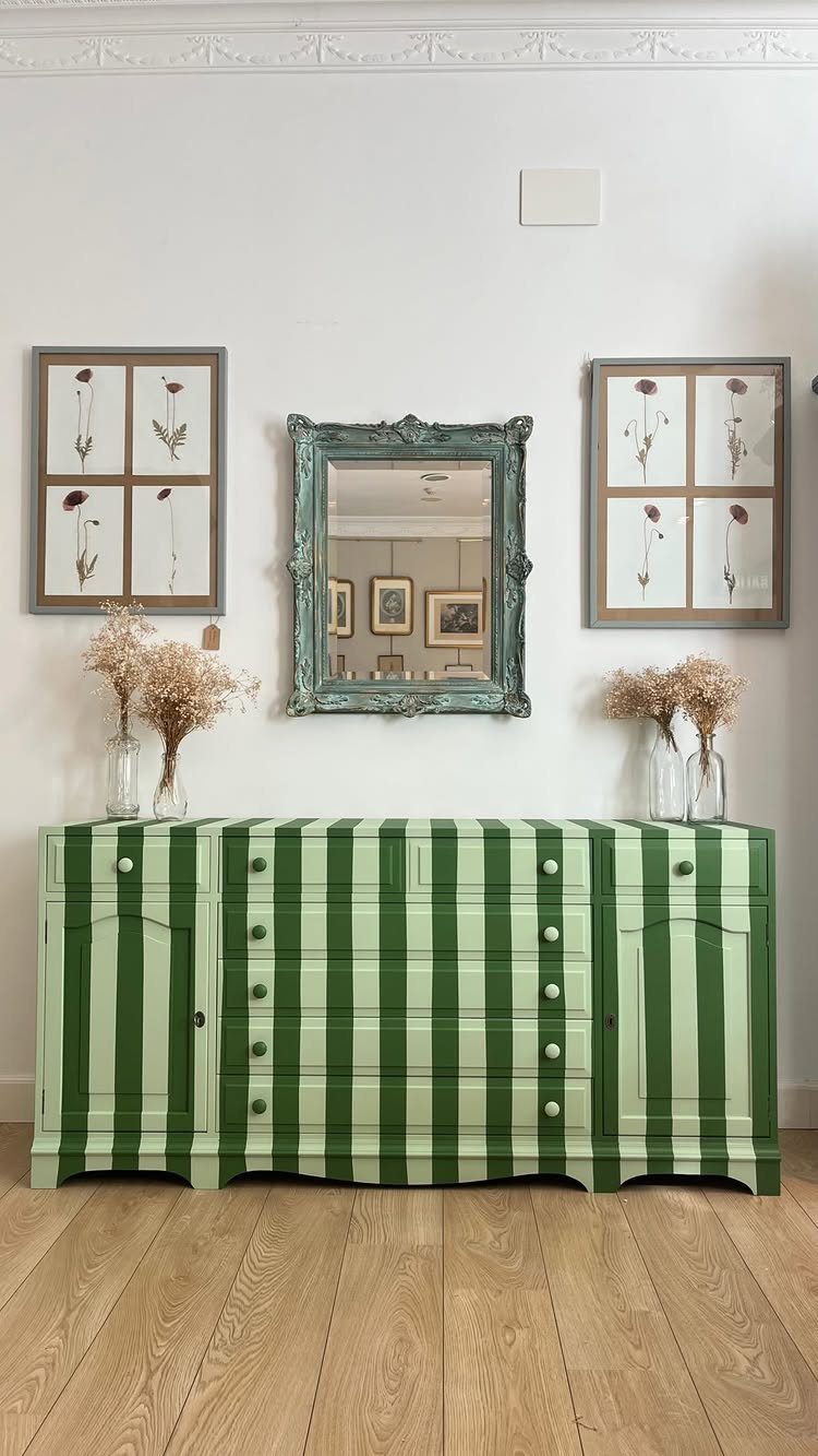 Green striped dresser with a teal mirror and botanical prints on a white wall.