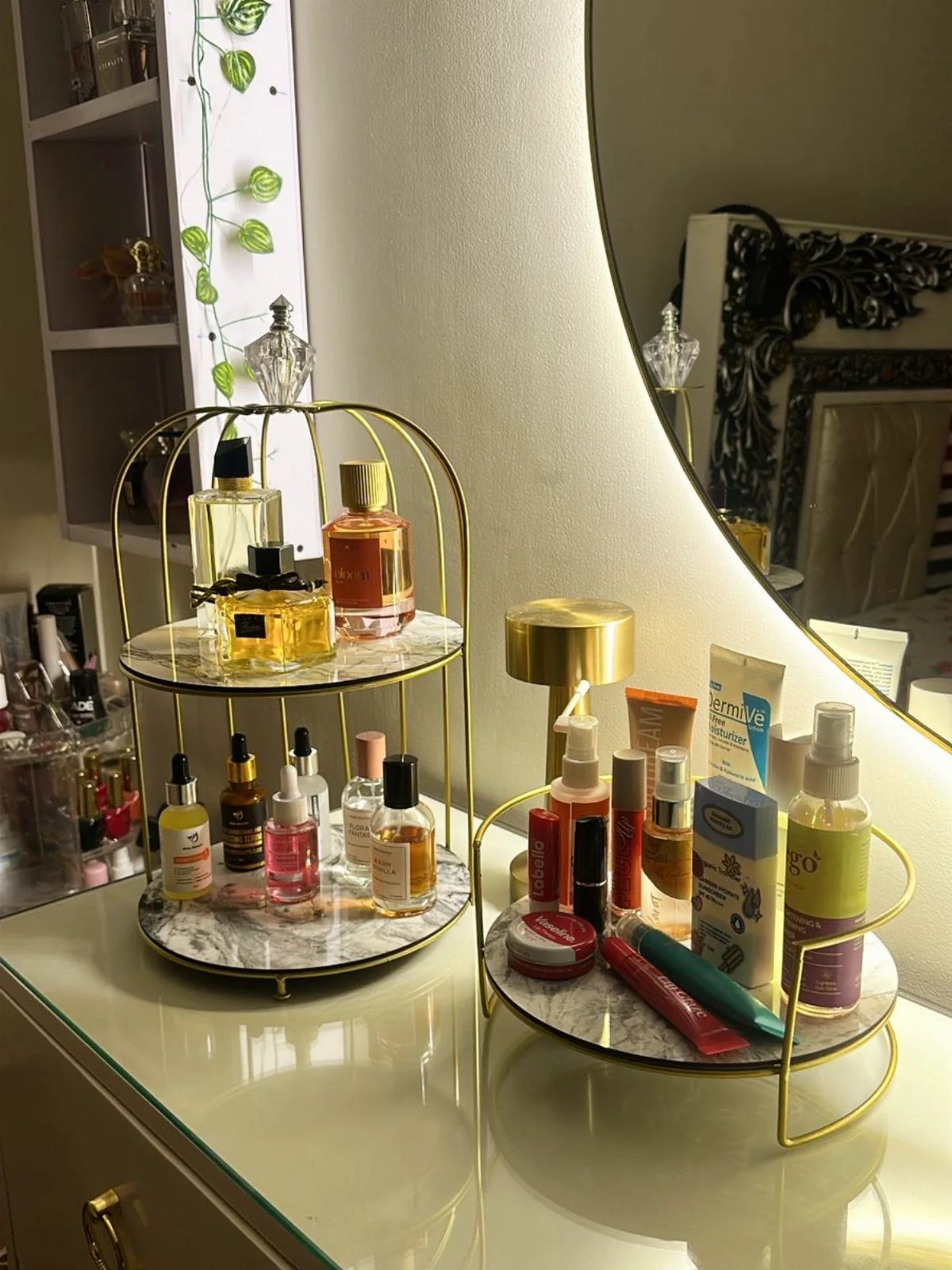 Gold metal trays with marble bases holding perfumes and skincare on a white dresser.