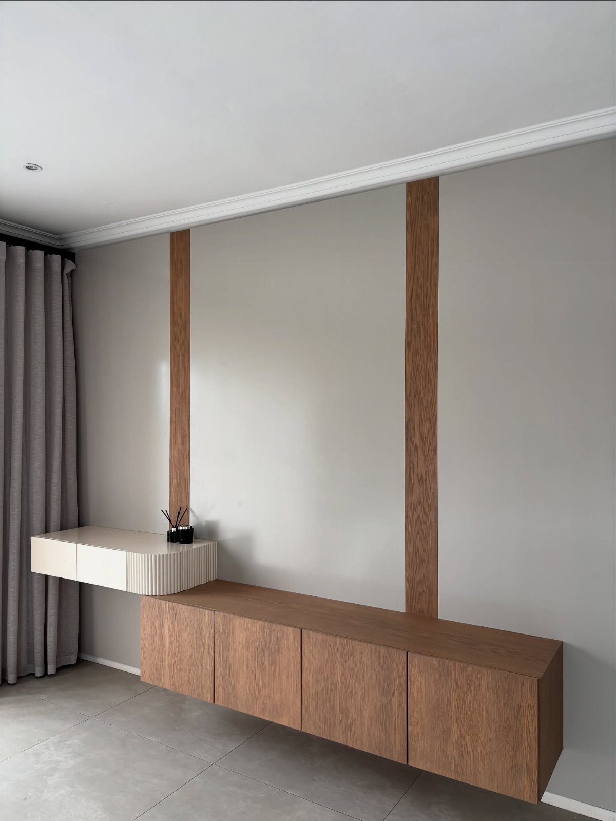 Floating wooden dresser and white side table against a grey wall with wooden slats.