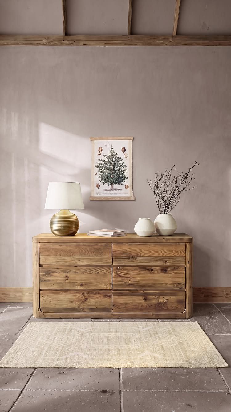 Wooden dresser with white minimalistic vases, a gold lamp, and framed tree art.