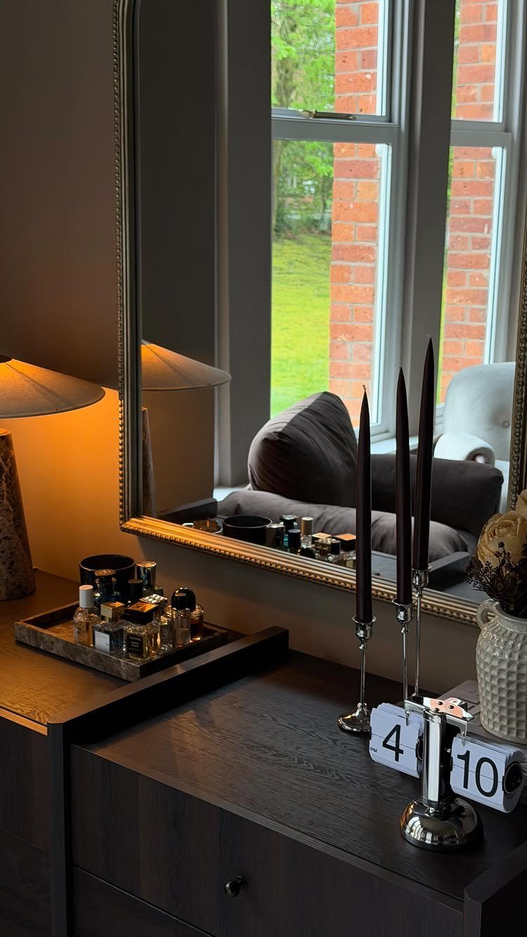 Large gold-framed mirror reflecting a window and sofa above a dark wood dresser.