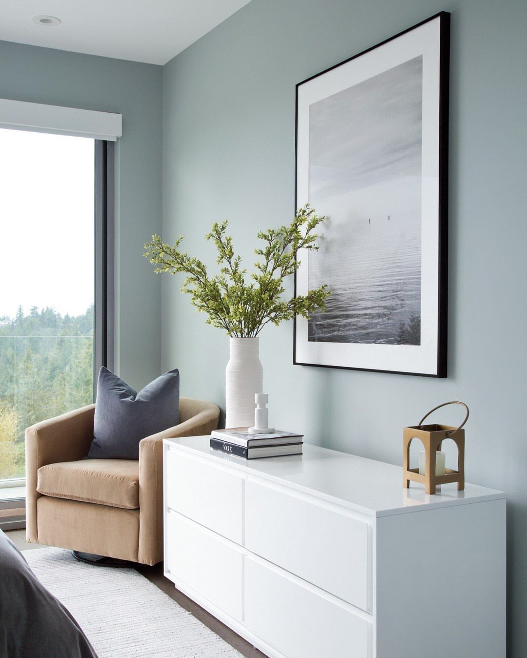 White modern dresser decorated with a vase of greenery and a wooden lantern.