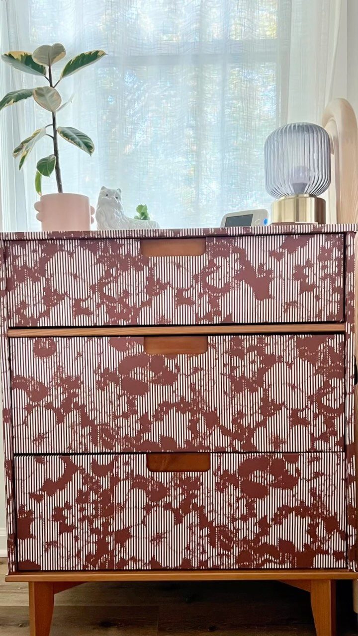 Patterned dresser drawers with a small plant and lamp on top against sheer curtains.