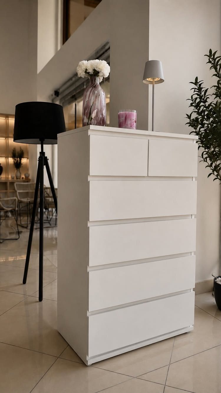 White modern dresser with a vase of white flowers and a grey lamp.