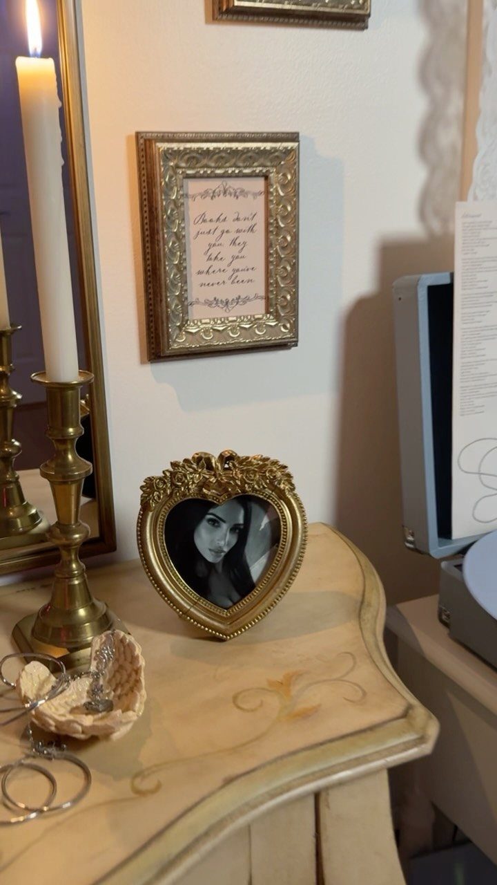 Vintage dresser top decorated with a gold heart frame, brass candle holder, and seashell.