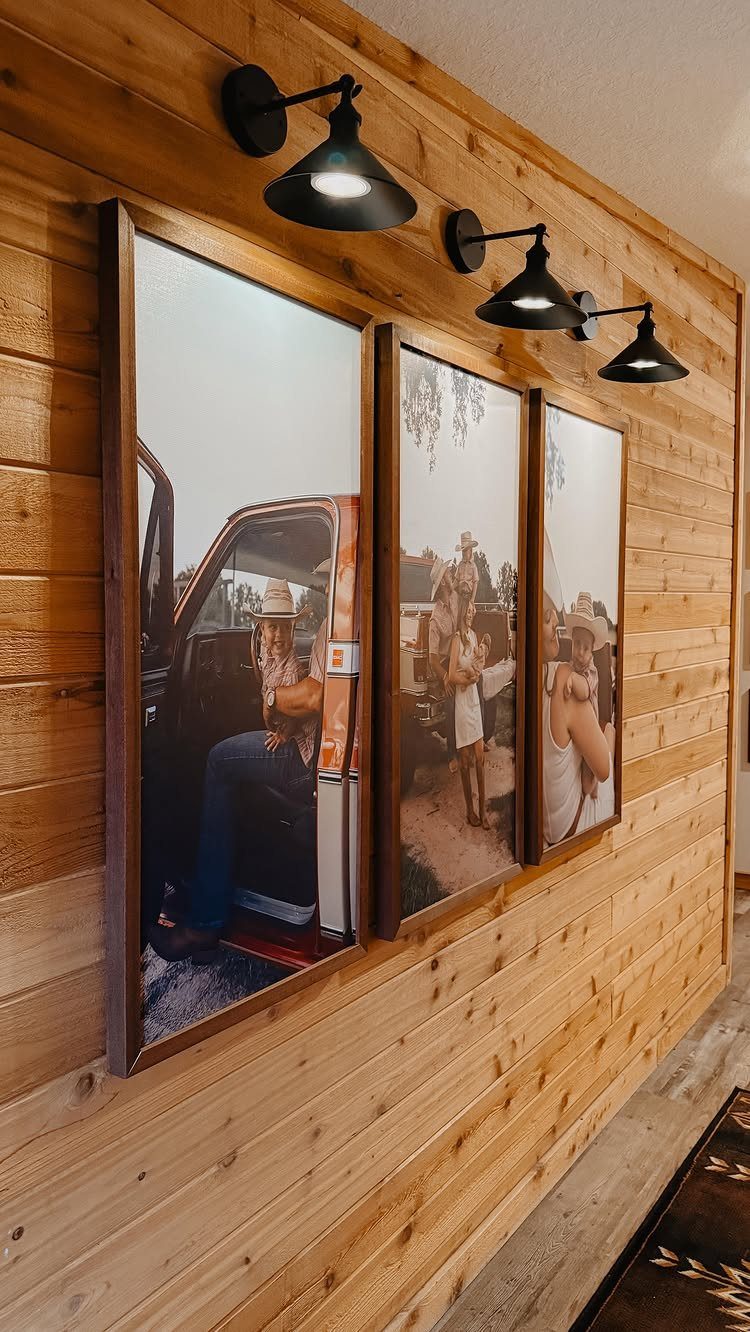 Three large framed rustic portraits on a light wood paneled wall with black sconces.
