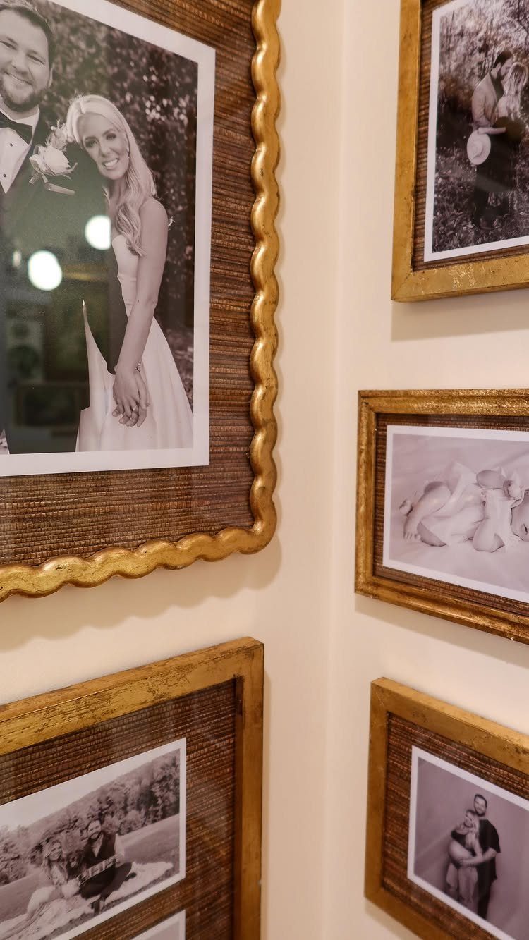Gold ornate frames with black and white family photos on a beige wall.