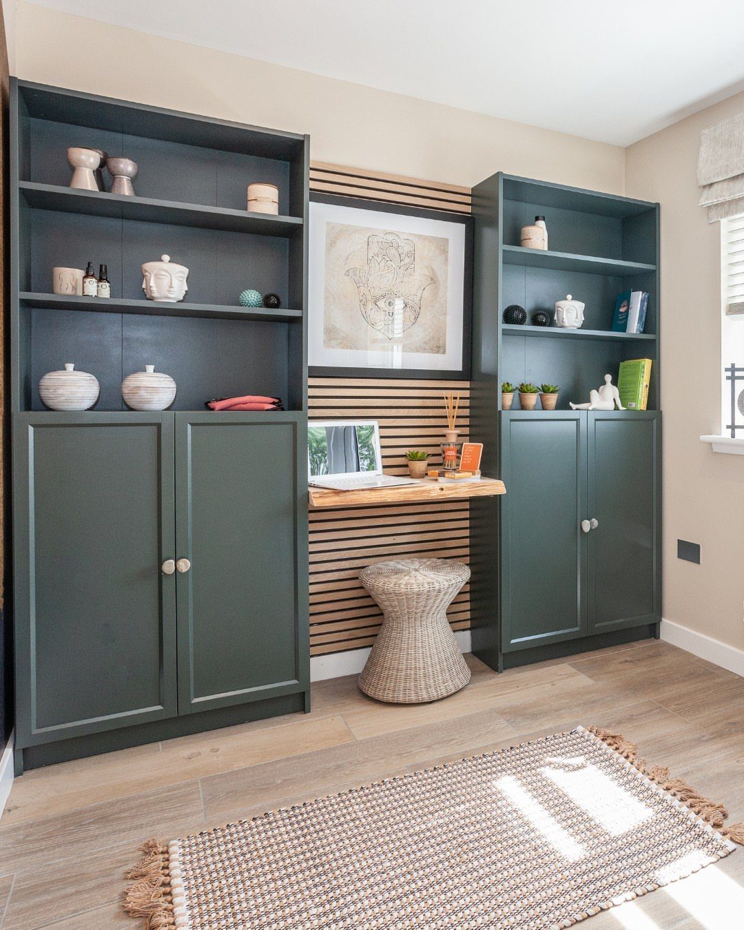Dark green built-in shelves and cabinets flanking a small wooden desk and wicker stool.