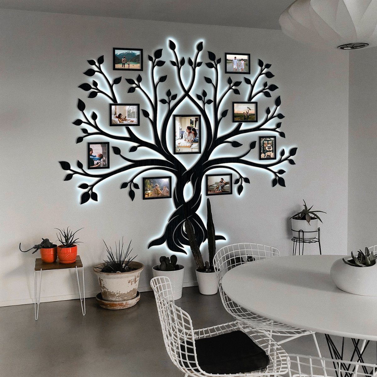 Tree-shaped wall sculpture with backlit branches holding small framed family photographs on white wall.
