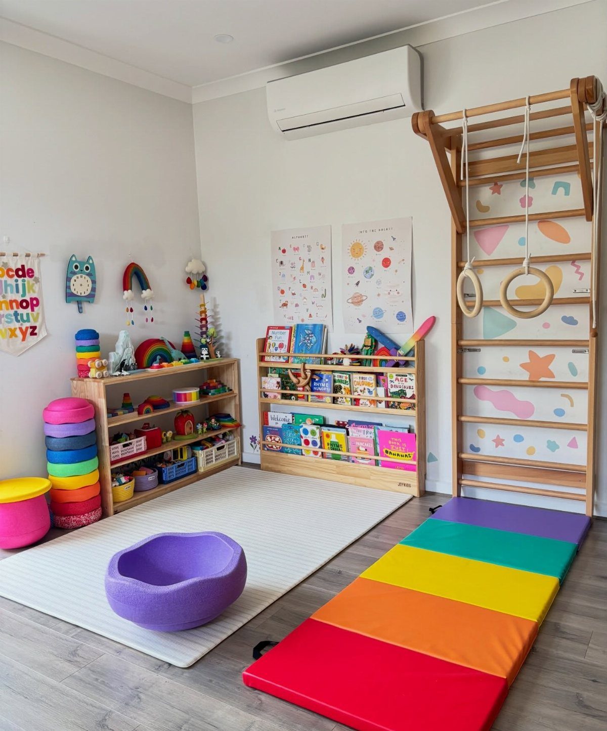 Children's play area with rainbow mat, climbing frame, and toy storage shelves.