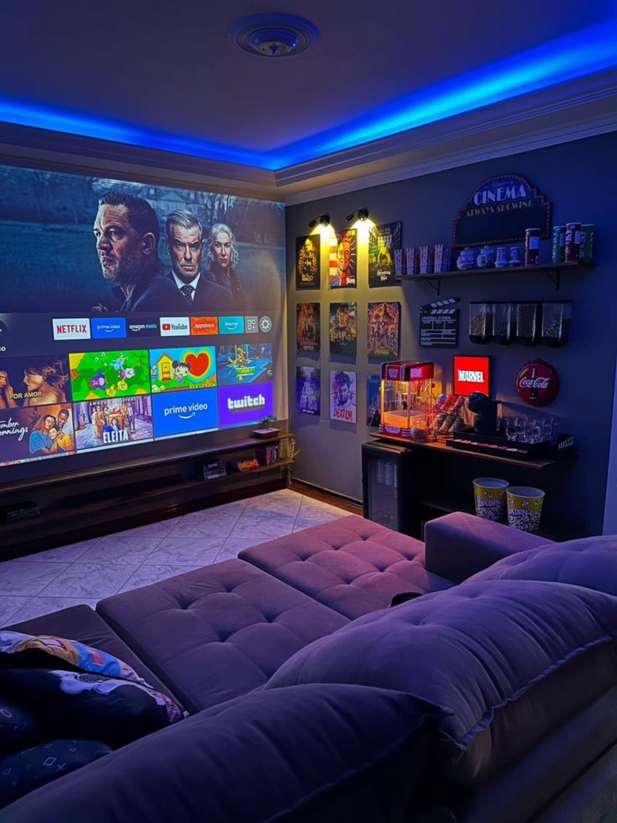 Home cinema room with large projection screen, purple sectional sofa, and snack station.