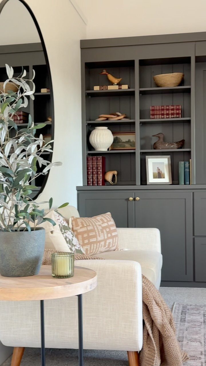 Dark grey built-in bookcase with decorative objects behind a cream colored sofa.
