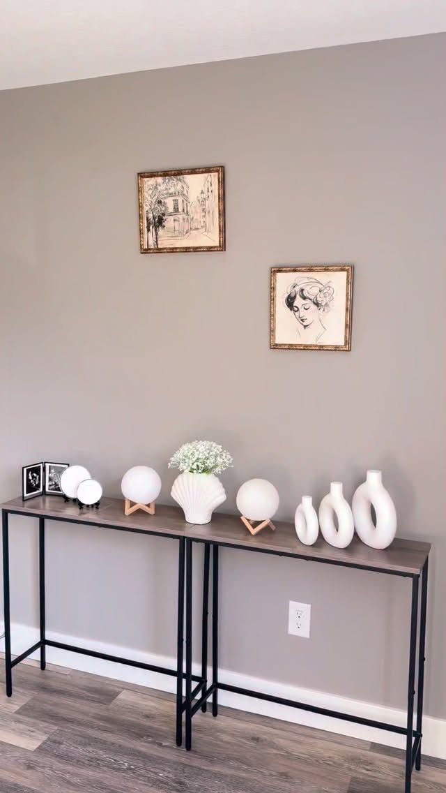 Console table with white decorative vases and spheres against a grey wall.
