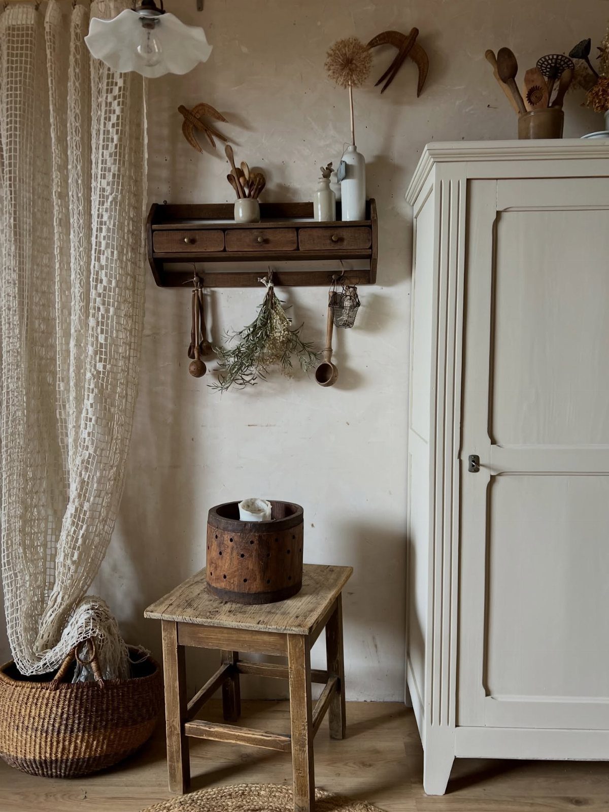 Cream wooden armoire and woven basket with lace curtain in rustic room