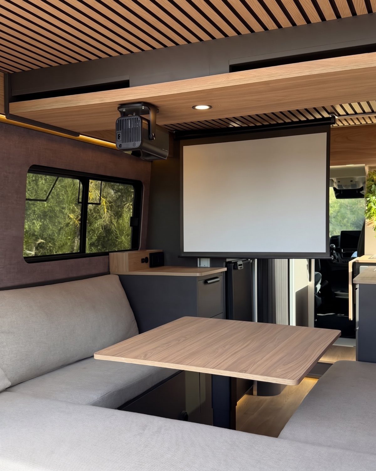Modern camper van interior with grey booth seating and a wooden dining table.