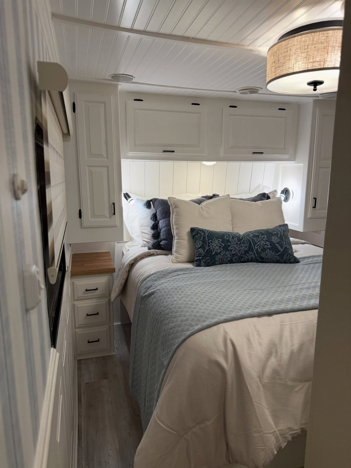 Bed with built-in white cabinets and bedside drawers inside a modern camper interior.