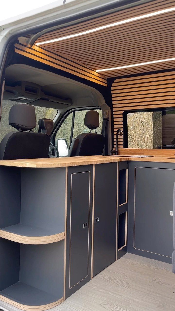 Custom grey cabinetry and slatted wooden ceiling inside a modern luxury camper van.