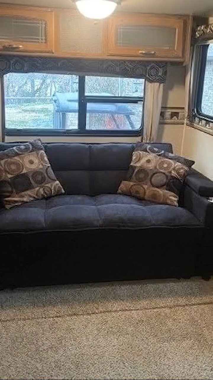 Dark blue sofa with patterned pillows inside a camper with wooden cabinets.