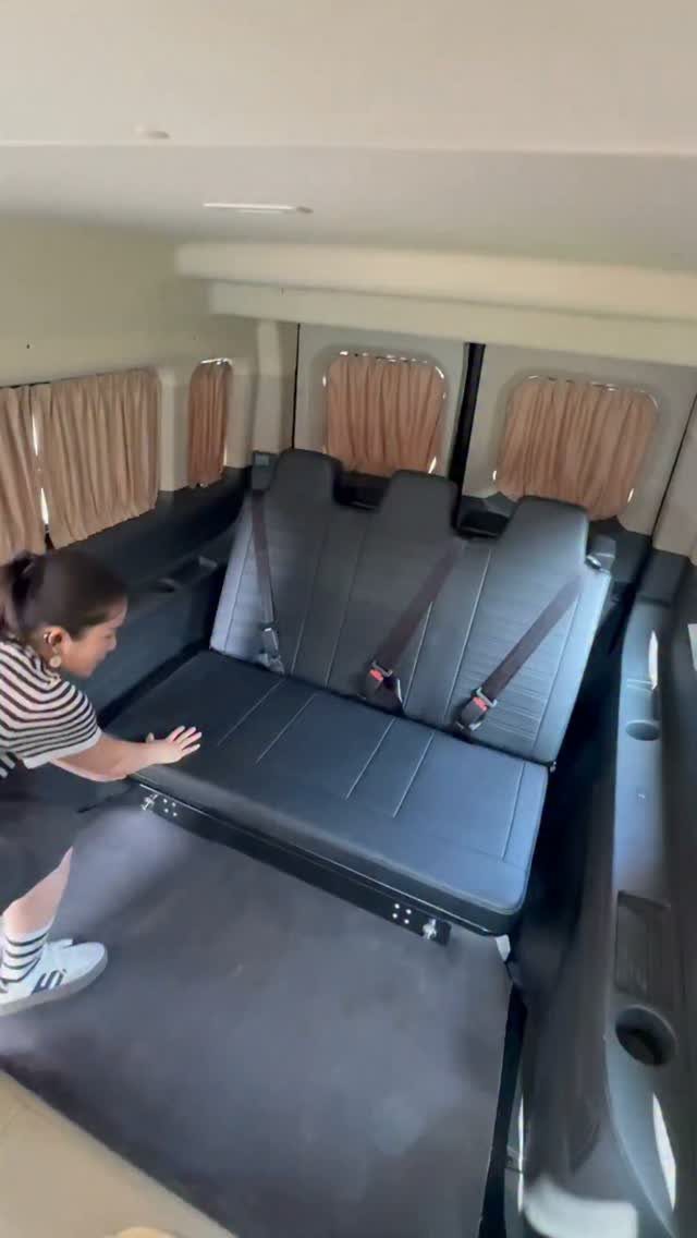 Black folding bench seat inside a camper van with a woman nearby.