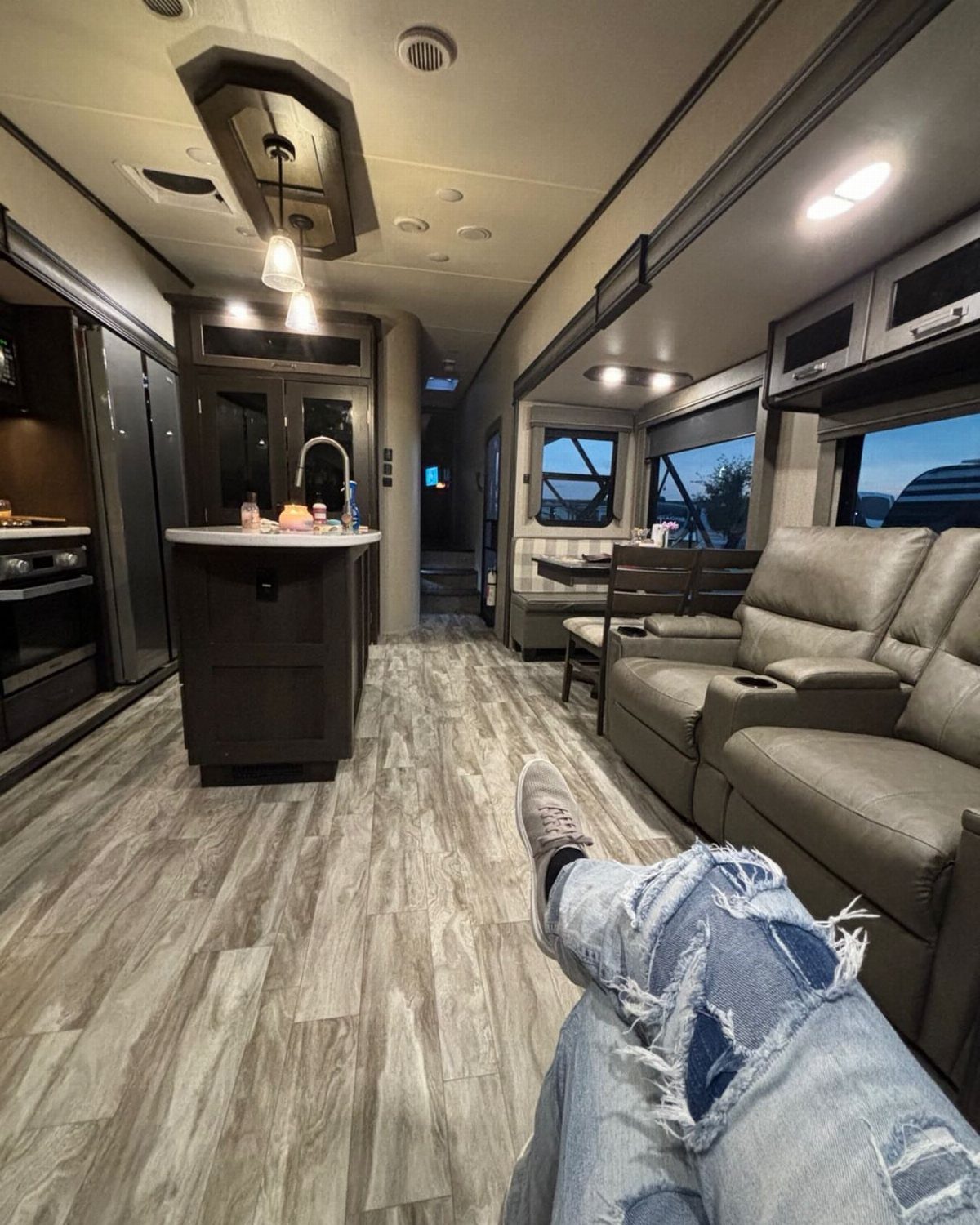 Modern RV interior with leather reclining sofas and a dark wood kitchen island.